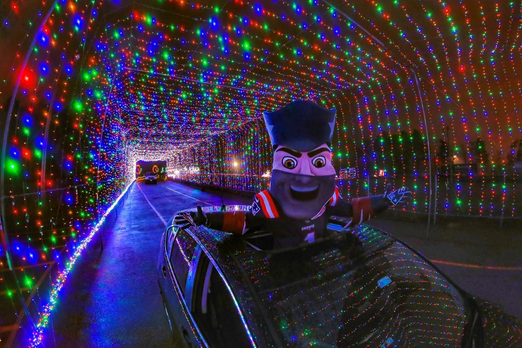 This is an image of Pat Patriot sticking out of a black cars sunroof. The car is driving through a tunnel of LED lights.