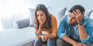 a man and woman looking at a pregnancy test struggling with infertility, the space we hold
