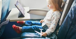 toddler sitting on an airplane watching an ipad and holding a toy airplane - tips for going on vacation with a toddler
