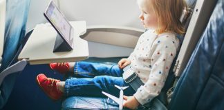 toddler sitting on an airplane watching an ipad and holding a toy airplane - tips for going on vacation with a toddler