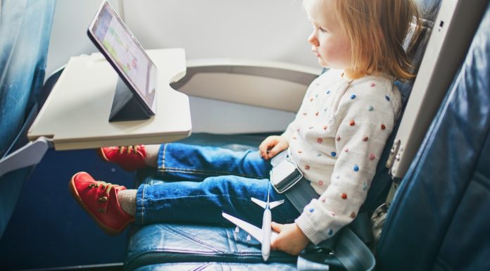 toddler sitting on an airplane watching an ipad and holding a toy airplane - tips for going on vacation with a toddler