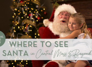 Santa Claus hugging a smiling little girl on his knee in front of a brightly lit Christmas tree.