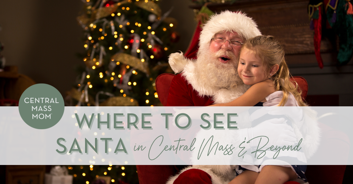 Santa Claus hugging a smiling little girl on his knee in front of a brightly lit Christmas tree.