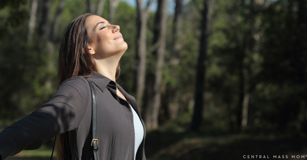 woman taking in a deep calming breath outdoors facing into the sunlight