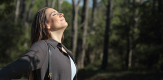 woman taking in a deep calming breath outdoors facing into the sunlight