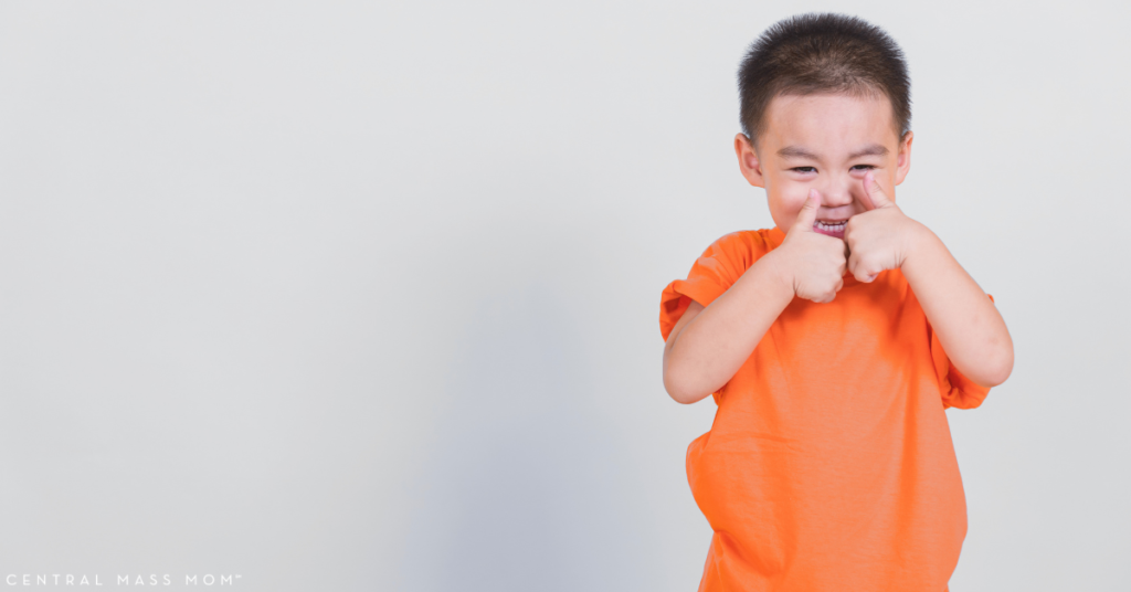 child holding two thumbs up wearing a bright orange shirt