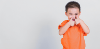 child holding two thumbs up wearing a bright orange shirt