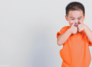 child holding two thumbs up wearing a bright orange shirt