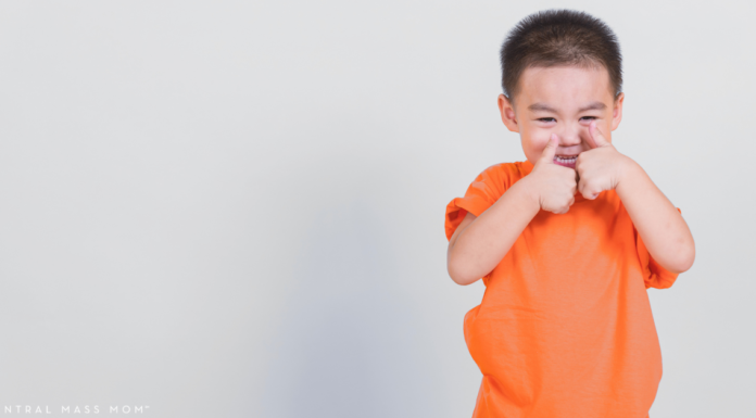 child holding two thumbs up wearing a bright orange shirt